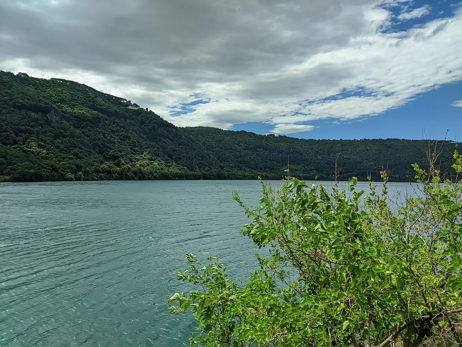 Il lago Albano con le sponde boscose del cratere e, in alto sulla cresta, gli edifici di Castel Gandolfo