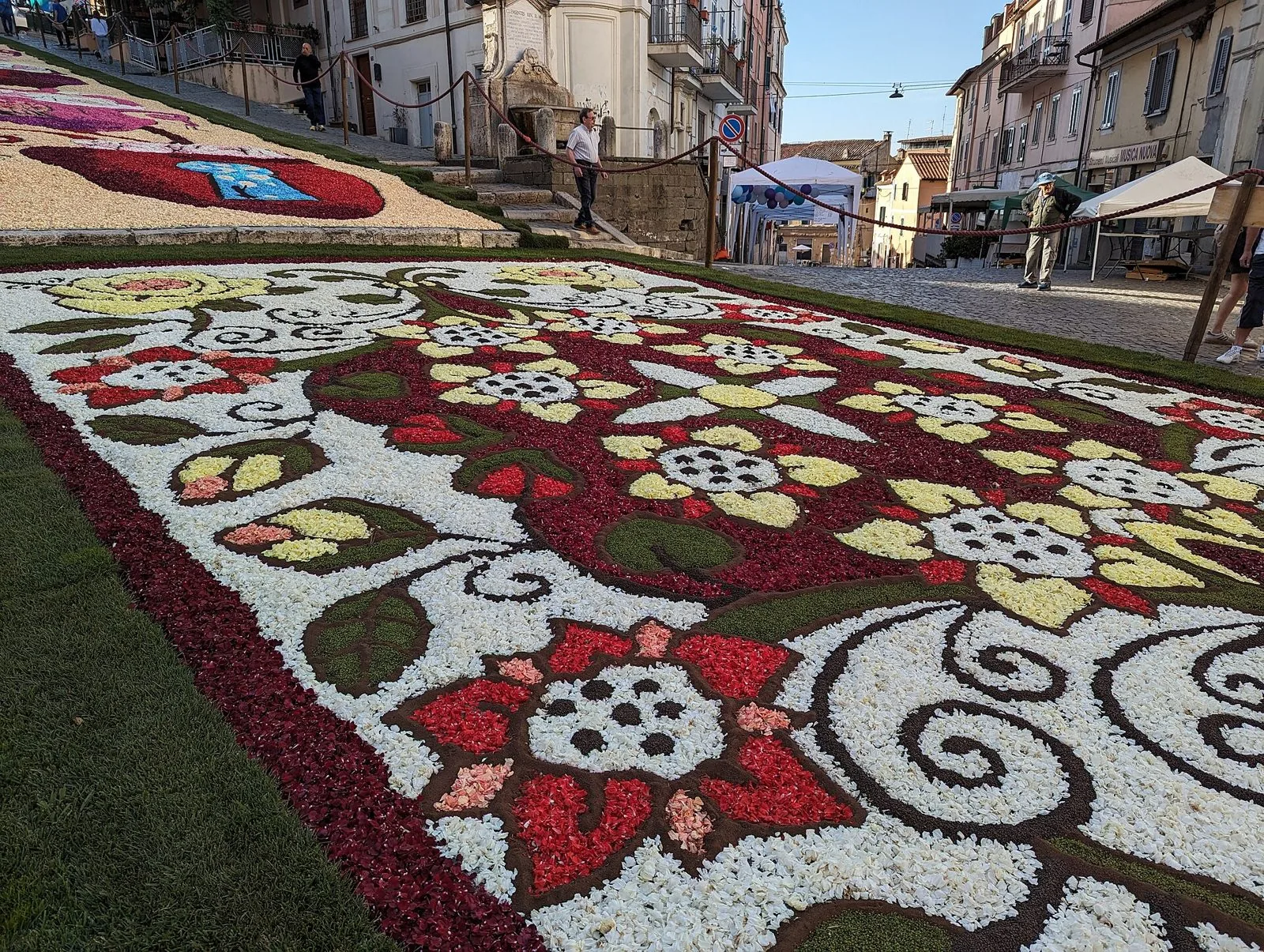 Quadro di petali bianchi, rossi e gialli con motivi floreali stesi sulla via in salita durante l'Infiorata di Genzano di Roma