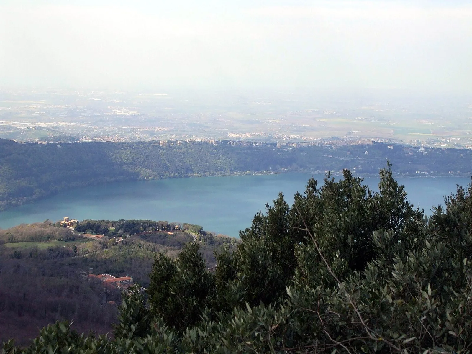 Il lago Albano visto dall'alto di Monte Cavo, con Castel Gandolfo sul bordo del cratere e la pianura verso Roma sullo sfondo